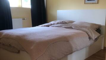 Une chambre à coucher avec un lit, un radiateur, une fenêtre avec des rideaux et un tableau encadré au mur.