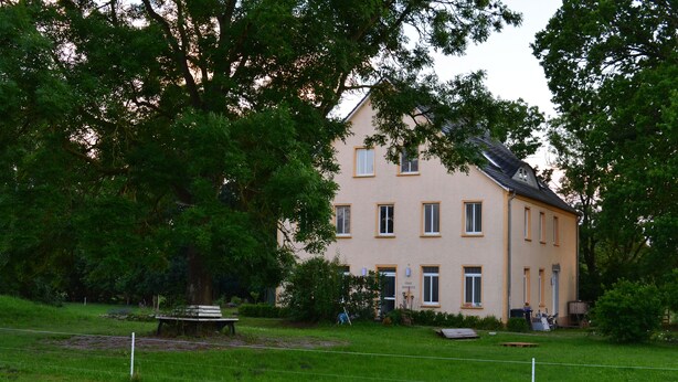 A two-story building with a symmetrical facade, a central entrance, and a small front garden with a bench. - Pferdehof Muhlitz on Rügen, an idyll for individualists (Samtens)