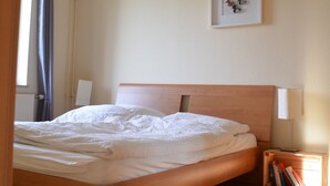 A bedroom with a wooden bed, a bedside table with books, a framed picture on the wall, and a window with curtains. - Pferdehof Muhlitz on Rügen, an idyll for individualists (Samtens)