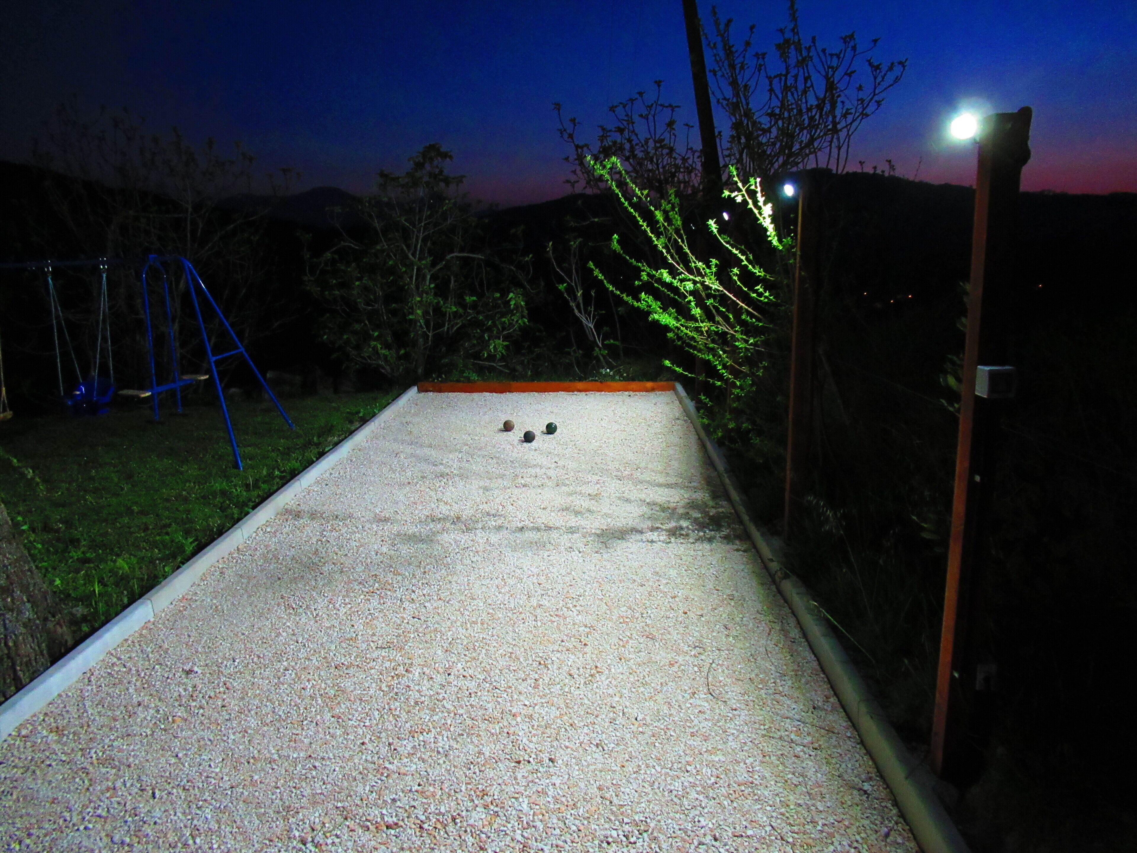 A shuffleboard table with three pucks, a blue swing set, and a street lamp in a backyard at dusk.