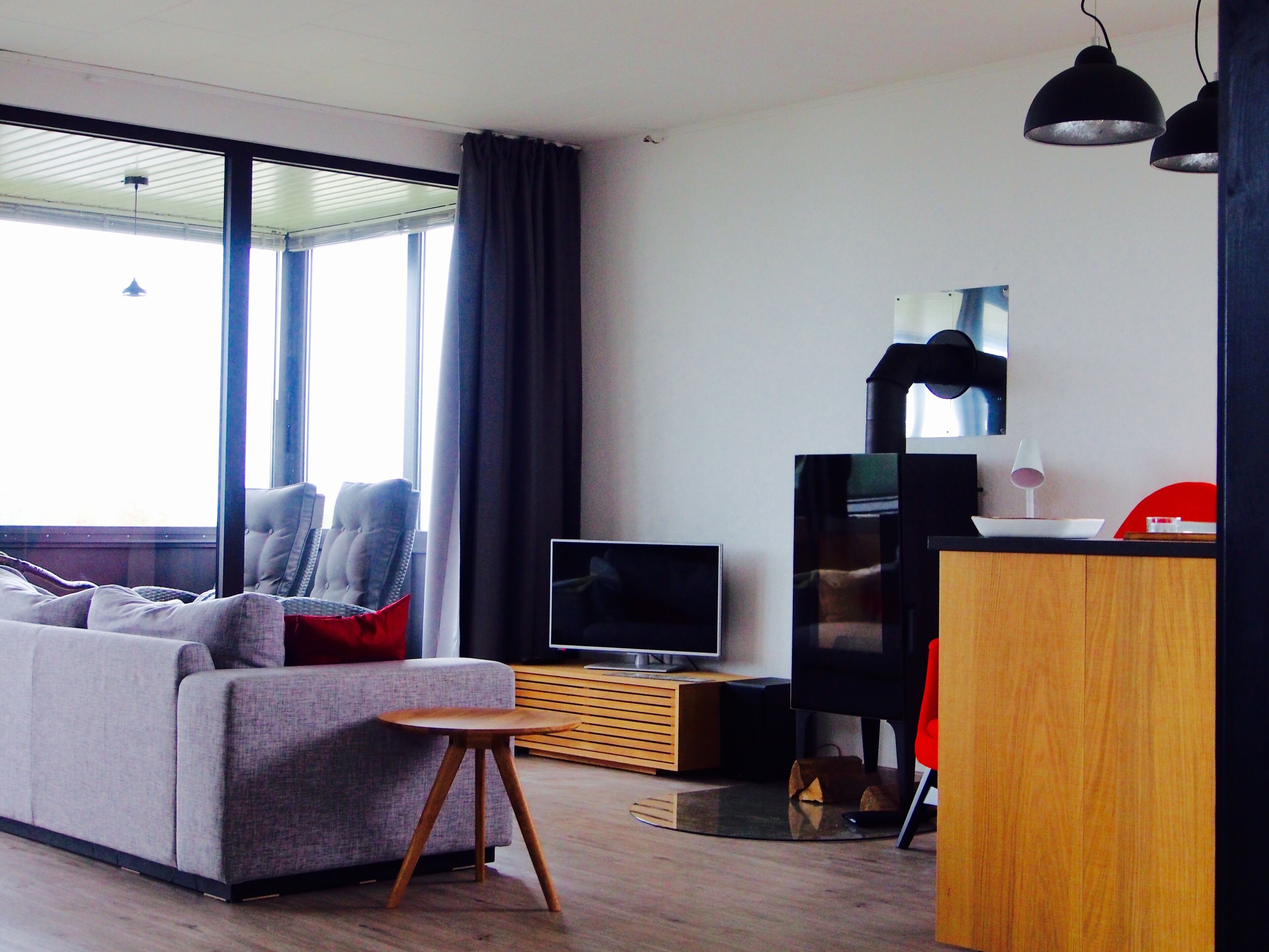 Ett modernt vardagsrum med en grå soffa, ett litet träbord, en tv och en matplats med en röd stol.