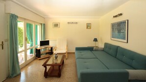 A living room with a blue sofa, a wooden coffee table, a TV on a stand, a chair, and a painting on the wall. - Casa Bella: A charming apartment with a beautifully overgrown garden (Bardolino)