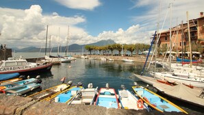 A marina with boats docked, a building with a red roof, and a mountain in the background. - Casa Bella: A charming apartment with a beautifully overgrown garden (Bardolino)