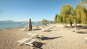 A pebble beach with lounge chairs and umbrellas, a clear sky, and a calm body of water. - Casa Bella: A charming apartment with a beautifully overgrown garden (Bardolino)