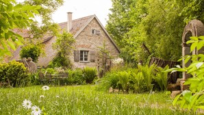 Une charmante maison en pierre avec un toit de tuiles, entourée d’une végétation luxuriante et d’un jardin.