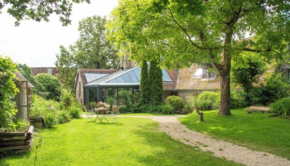 Un jardín cuidado con un patio, un invernadero y una casa tradicional con techo inclinado.