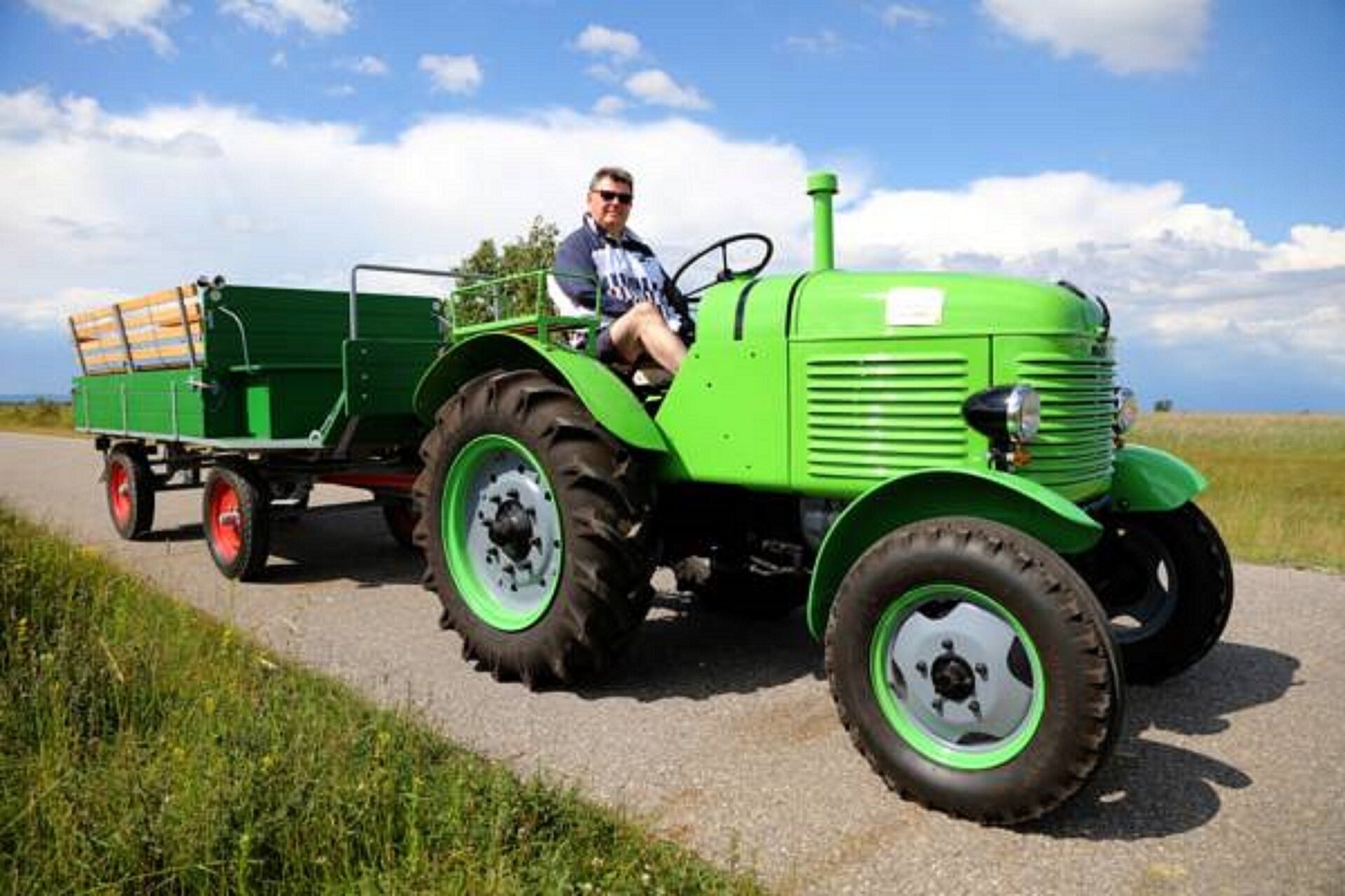 A green tractor with a trailer on a rural road.