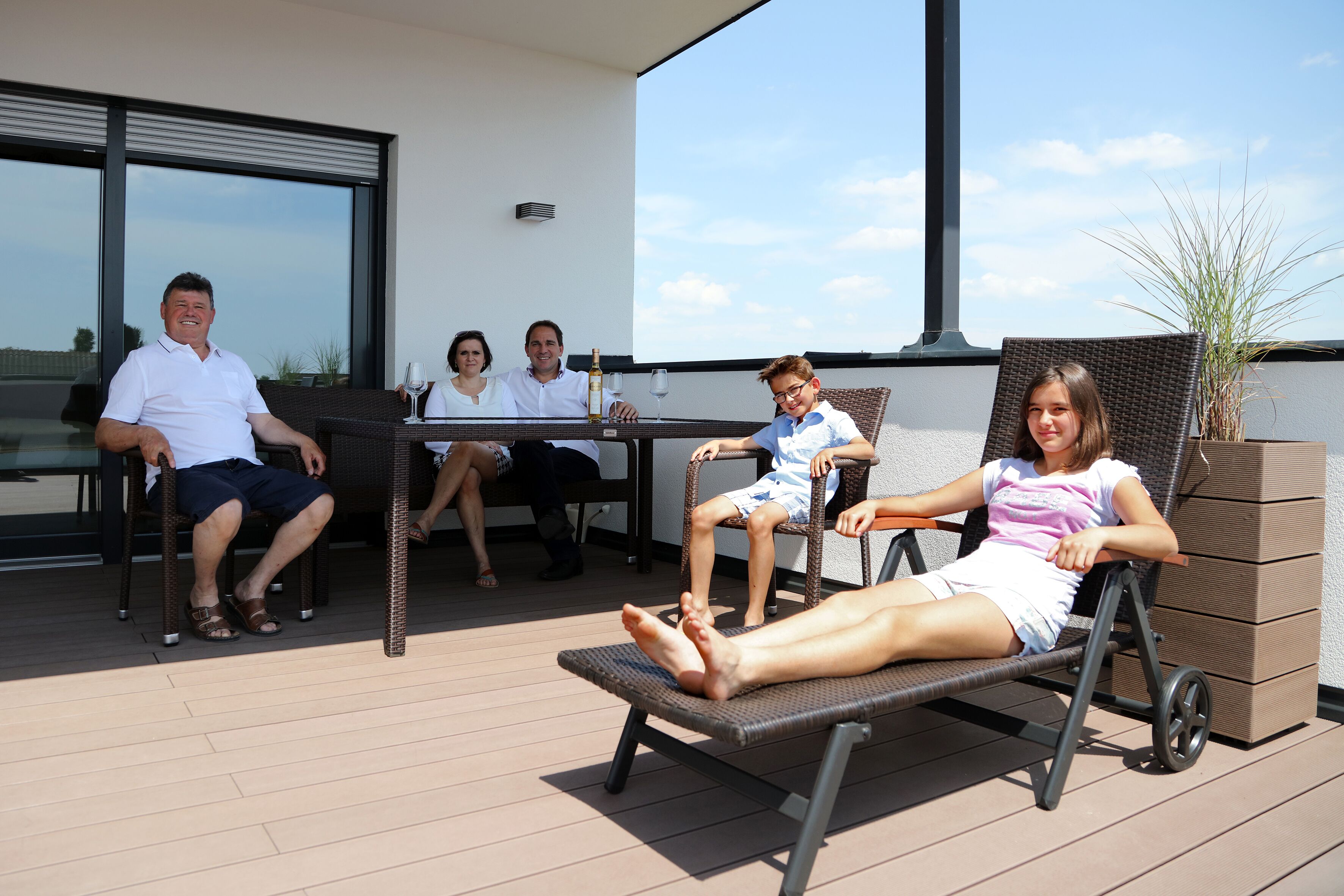 A family of four on a deck with a table, chairs, and a potted plant.