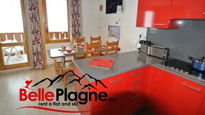 A modern kitchen with red cabinets, a flat-screen TV, and a dining area with wooden chairs and a table. - Calysto, 3 *, Heart of Belle-Plagne, on the slopes (La Plagne Tarentaise)