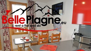 A modern kitchen with red cabinets, a stainless steel refrigerator, and a dining area with wooden chairs and a table. - Calysto, 3 *, Heart of Belle-Plagne, on the slopes (La Plagne Tarentaise)
