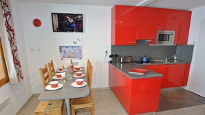 A modern kitchen with red cabinets, a built-in microwave, and a dining area with wooden chairs and a table set for six.