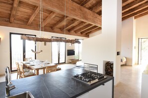 A modern kitchen with a central island, wooden ceiling beams, and a dining area with natural light.