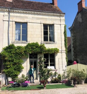A two-story building with a symmetrical facade, large windows, and a small garden area with potted plants and a table.