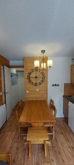 Een houten eettafel met stoelen, een wandklok en een kroonluchter.