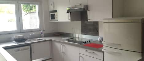 Una cocina moderna con armarios blancos, un microondas empotrado, una estufa a gas y un refrigerador.