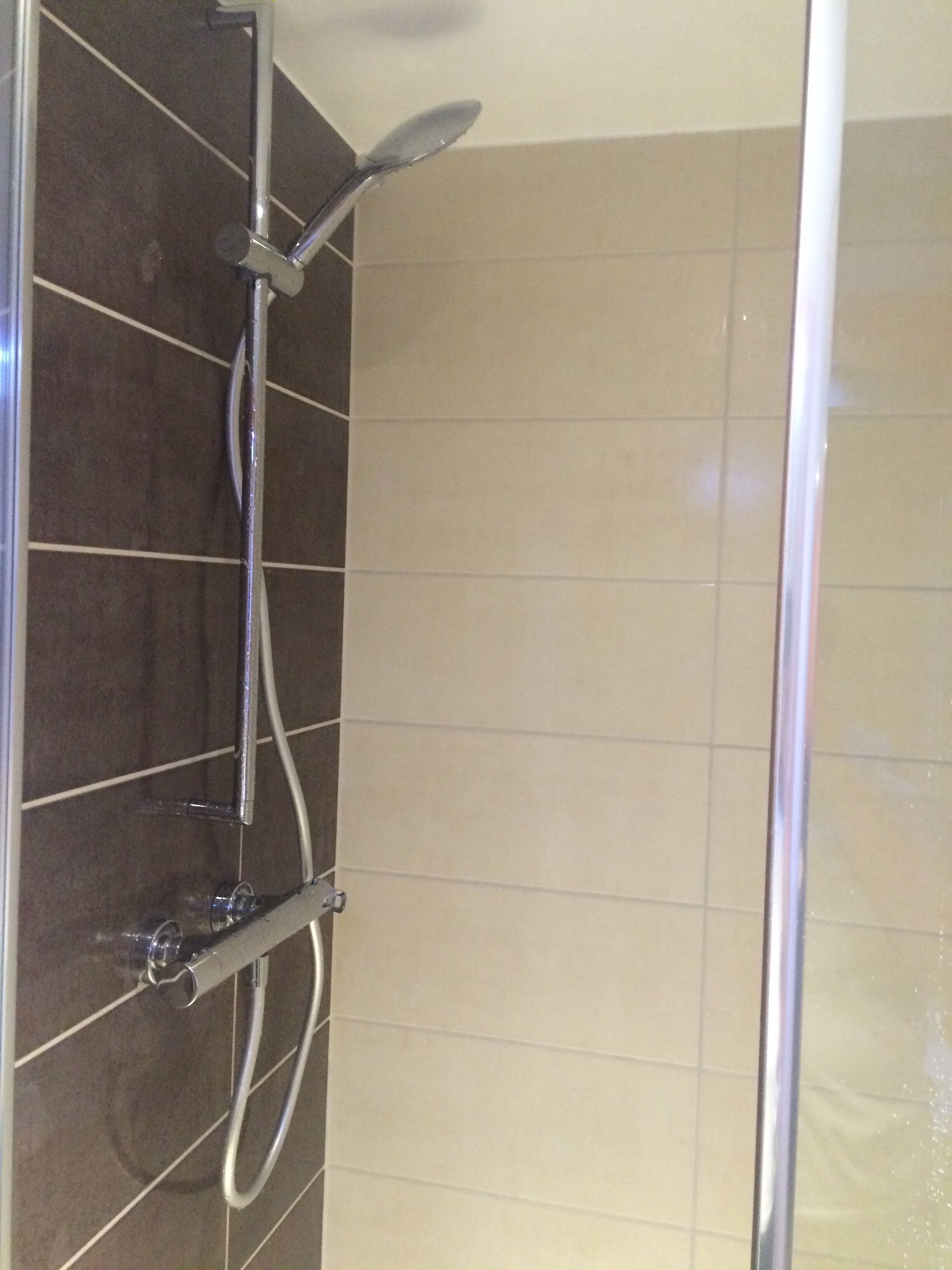 A shower with a handheld showerhead and a wall-mounted control panel.