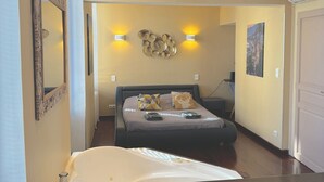 Quarto de hotel com cama, mesas de cabeceira, espelho, luminárias na parede e um quadro.