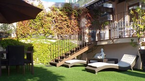 Um jardim no terraço com grama sintética, móveis de exterior e uma escadaria que leva a um nível superior.