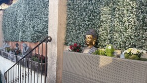 Escadaria com corrimão de metal que leva a uma área coberta, onde se vê uma estátua de Buda e uma parede coberta por vegetação.