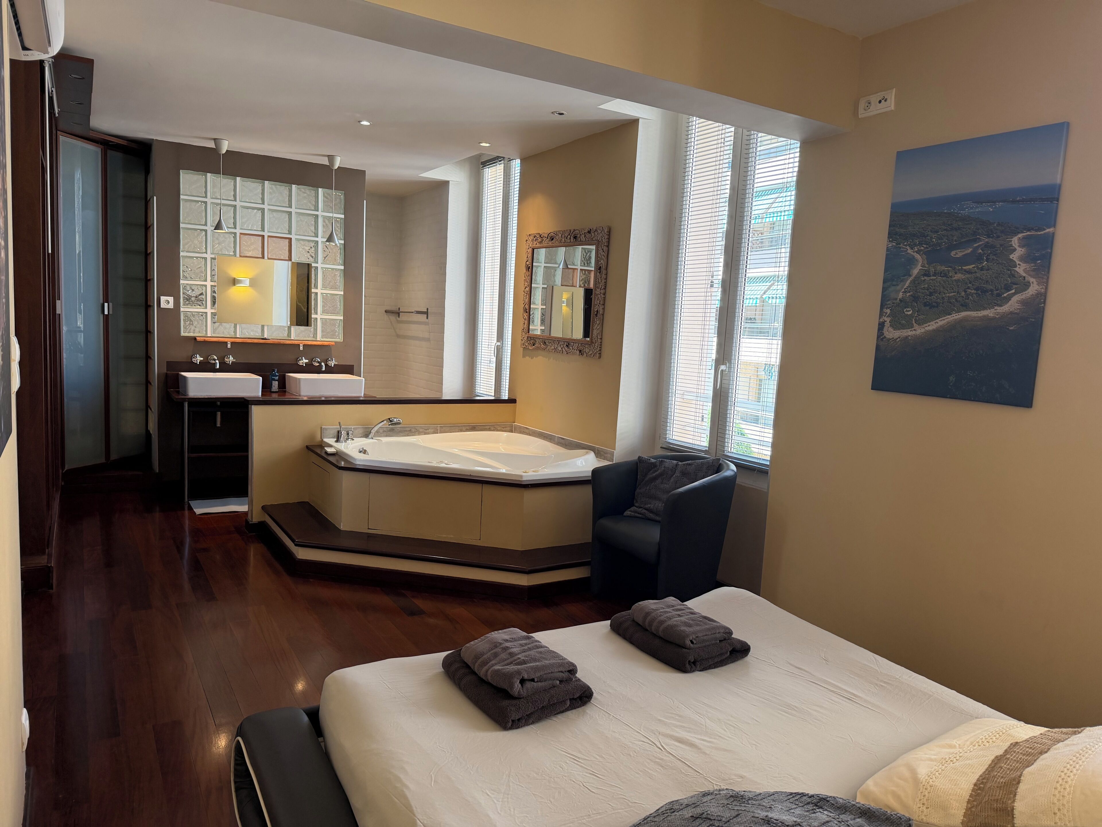 Una camera d'albergo con un letto grande, un'area salotto, un bagno con vasca e vista sul mare dalle finestre.