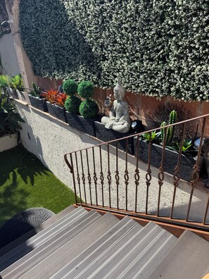 Un escalier doté d’une rampe métallique mène à un espace jardin agrémenté de diverses plantes et d’une statue.