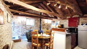 A rustic kitchen with a stone wall, wooden ceiling beams, and a dining area with a table and chairs. - Eco-responsible cottage CASTAGNERE 4* EN CEVENNES: air conditioning, pets welcome (Aujac)