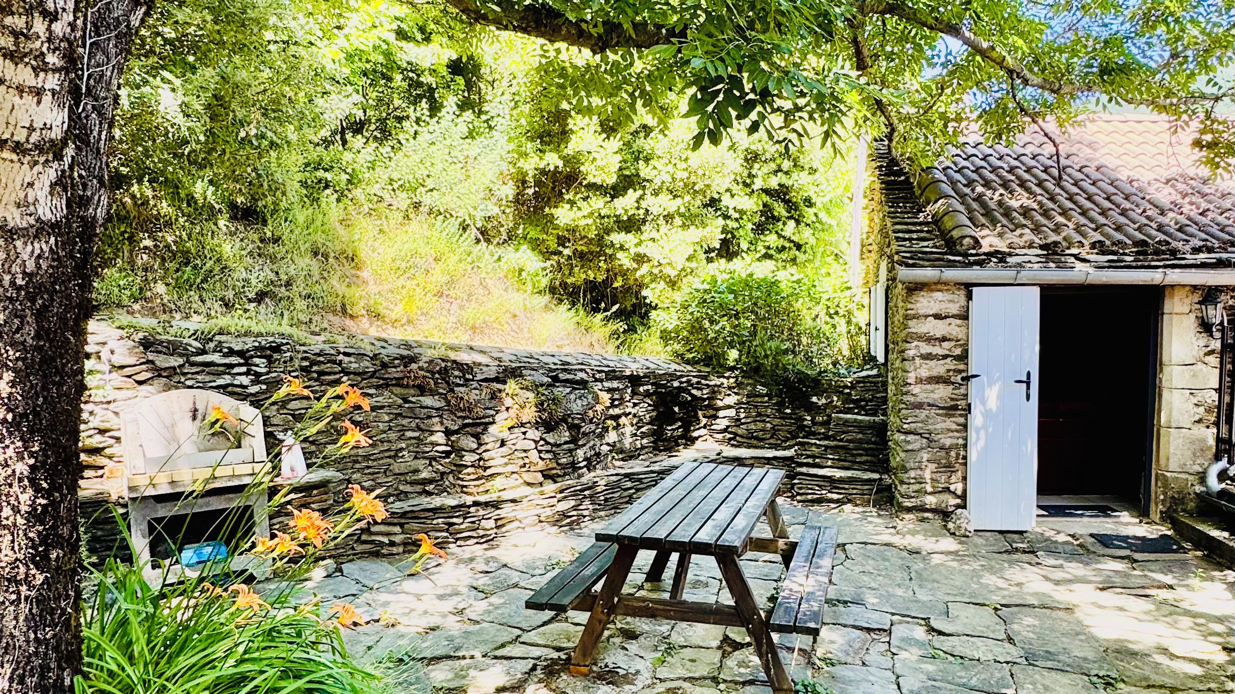 Un mur de pierre, un banc en bois et un petit bâtiment avec une porte.