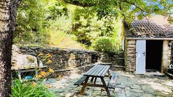 Un mur de pierre, un banc en bois et un petit bâtiment avec une porte.