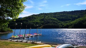 A lakeside view with kayaks and canoes docked, surrounded by lush greenery and hills. - Eco-responsible cottage CASTAGNERE 4* EN CEVENNES: air conditioning, pets welcome (Aujac)