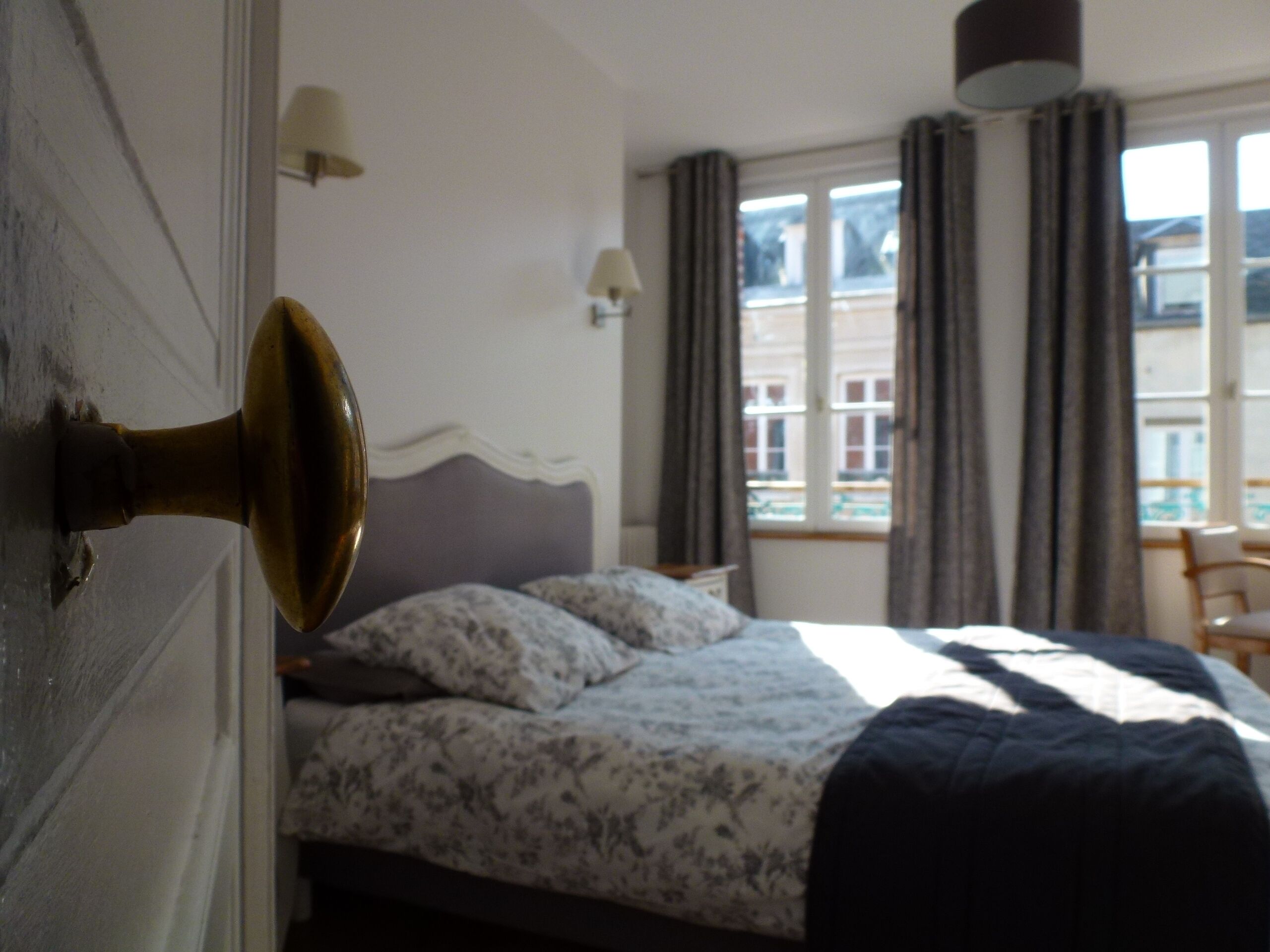 Une chambre à coucher avec un lit, deux lampes de chevet, une fenêtre avec des rideaux et une vue sur les bâtiments à l’extérieur.