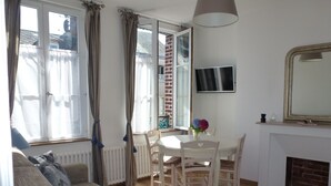 A cozy living room with a sofa, a dining table with chairs, a TV, and a fireplace. - French Charm.  Charming 40-square-meter apartment.⭐️⭐️⭐️ (Honfleur)
