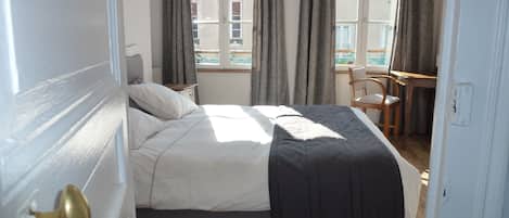 A bedroom with a bed, a chair, a desk, and a window with curtains.