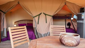 Una tenda con un letto a castello, un tavolo con una ciotola di legno e un frigorifero.