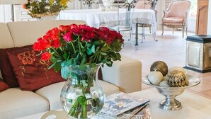 Una sala de estar acogedora con un sofá, una mesa de centro con un jarrón de flores rojas, y un comedor al fondo.