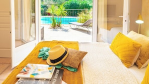 Un dormitorio con cama, una mesa de madera y vistas a una piscina y jardín.