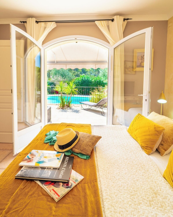 A bedroom with a bed, a wooden table, and a view of a pool and garden.