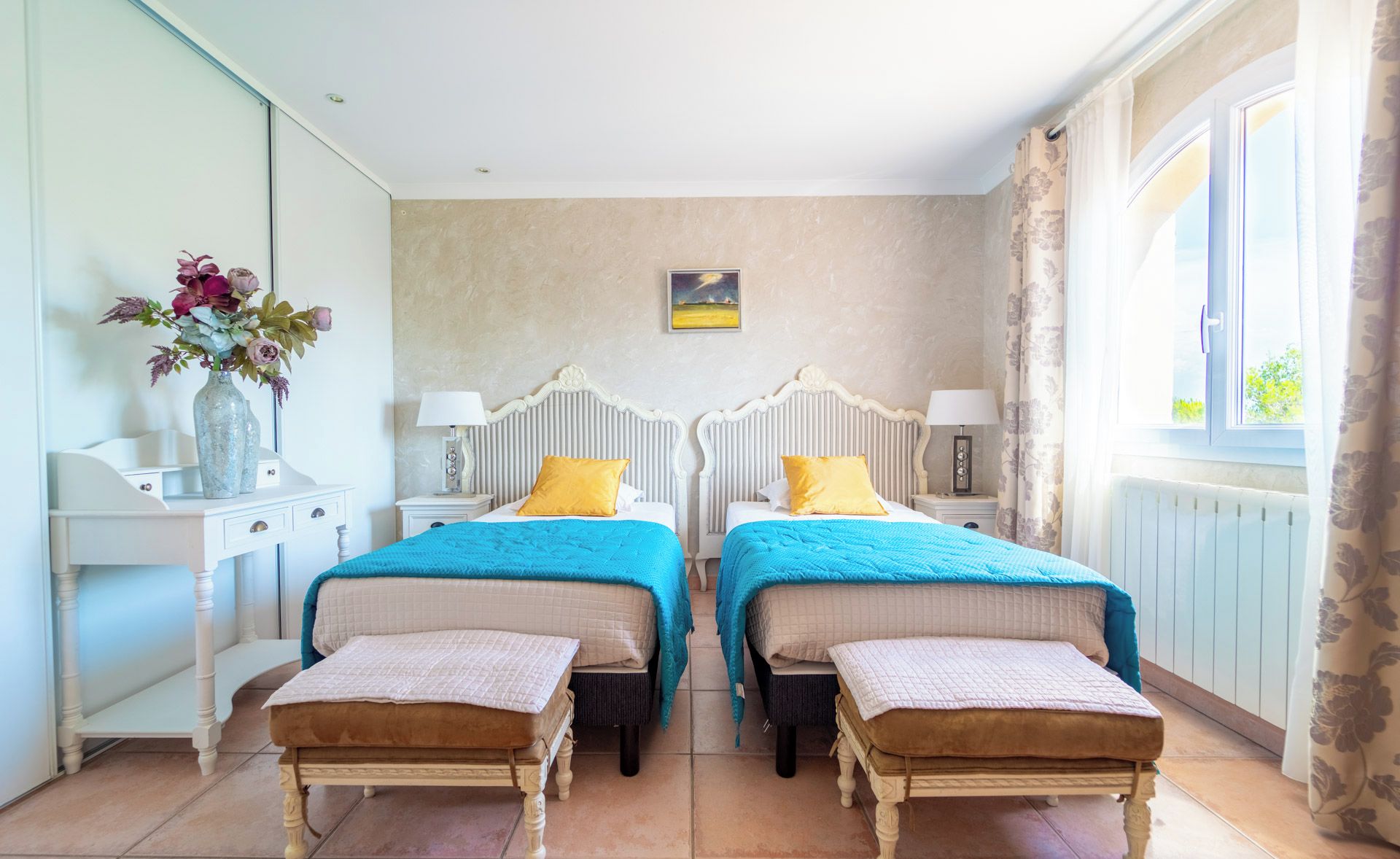 A double room with two beds, each with a headboard, bedside tables, lamps, and matching ottomans.