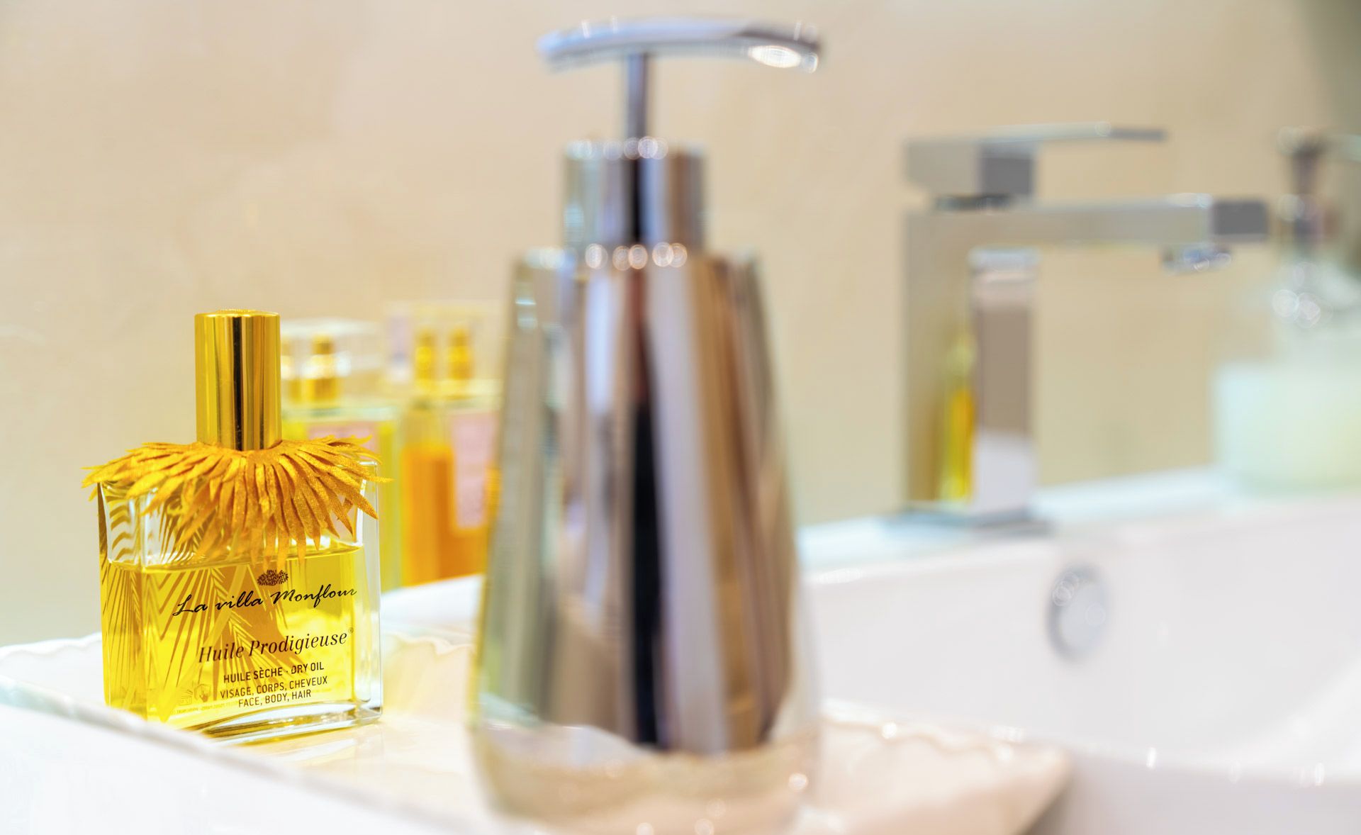 A bathroom sink with a gold-colored bottle of La villa Monflour oil and a silver faucet.