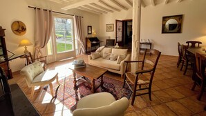 A spacious living room with a large window, a sofa, a coffee table, and a dining area with wooden chairs and a table.