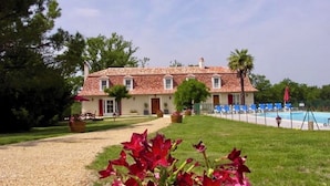 A two-story building with a tiled roof, a swimming pool, and a well-maintained lawn.