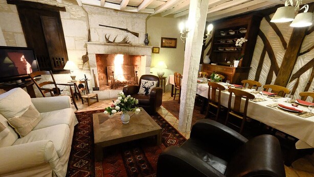 A cozy living room with a fireplace, a television, and a dining area with wooden chairs and a table set for a meal.