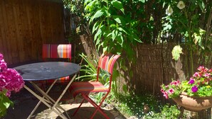 Terassi, jossa on pyöreä pöytä ja punainen tuoli, ja jonka ympärillä on vehreää kasvillisuutta sekä bambuaita.