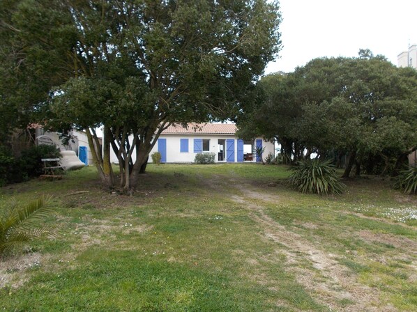 Une maison à l’extérieur blanc et aux volets bleus, entourée d’arbres et d’une pelouse.
