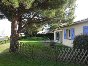 A house with a large tree in front, a wooden fence, and a small garden area.