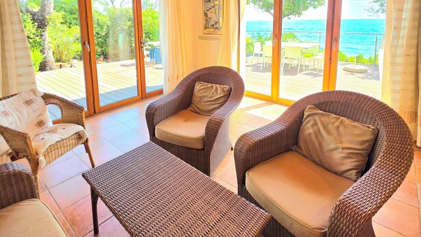 A room with wicker furniture, large sliding glass doors, and a wooden ceiling. - Small pariadis, feet in the water, raised ground, 10pers! (Zonza)