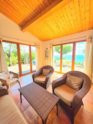A room with wicker furniture, large sliding glass doors, and a wooden ceiling. - Small pariadis, feet in the water, raised ground, 10pers! (Zonza)
