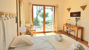 A bedroom with a bed, a desk, a chair, and a view of the outdoors. - Small pariadis, feet in the water, raised ground, 10pers! (Zonza)