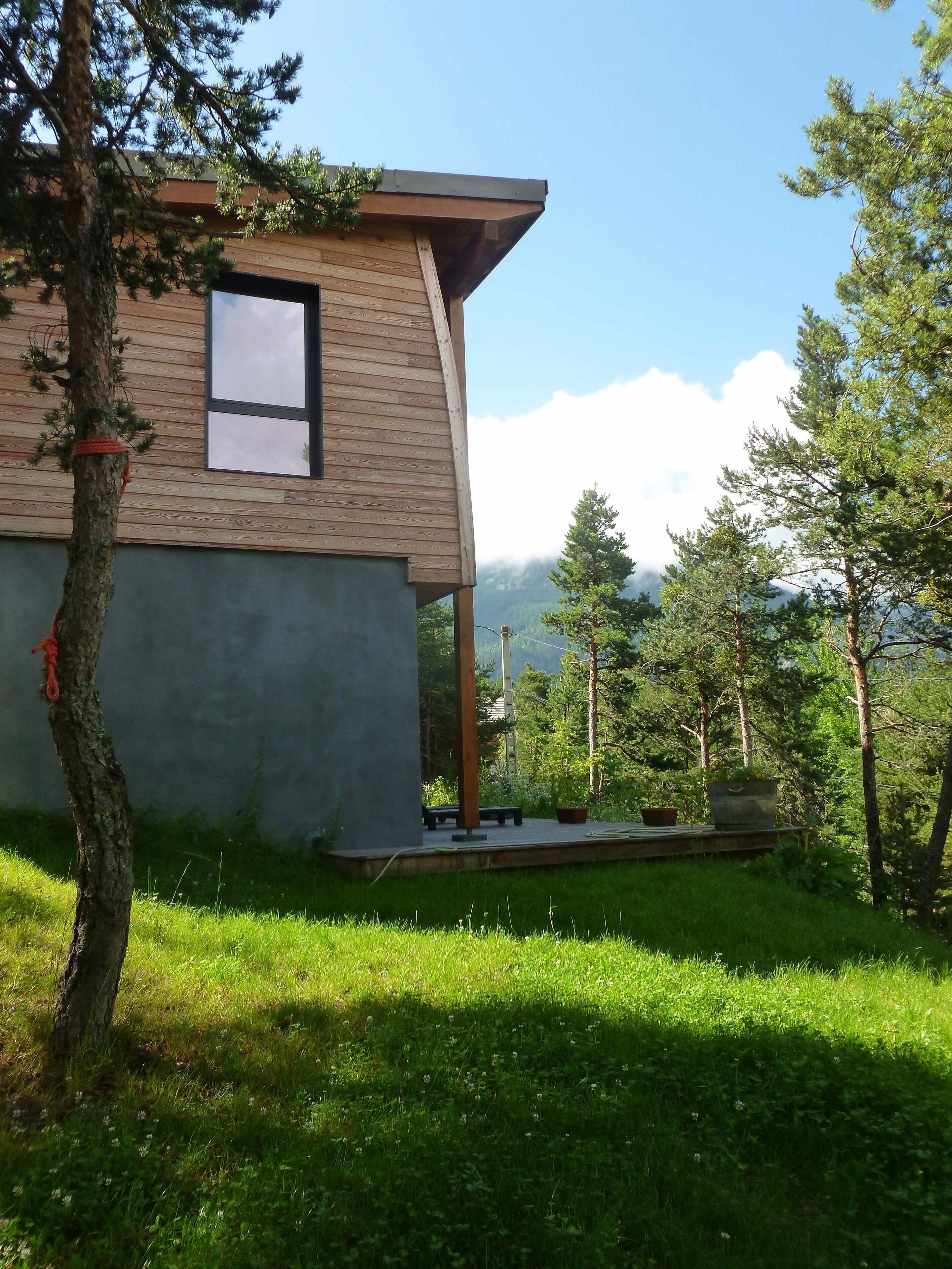 Un bâtiment moderne en bois, doté d’une grande fenêtre et entouré d’une végétation luxuriante et d’arbres.
