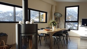 Une cuisine moderne dotée d’un poêle à bois, de grandes fenêtres offrant une vue sur les montagnes et d’un coin repas avec des chaises et une table.