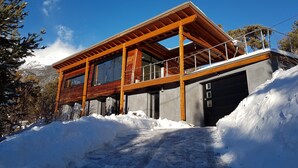 Une maison moderne dotée d’une terrasse en bois, de grandes fenêtres et d’un garage.